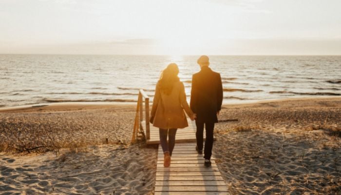 a couple walking down a pier on a sand beach